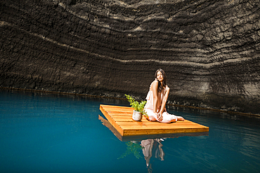 Portrait of woman sitting on floating dock near rocky coast