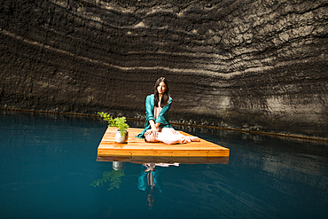 Portrait of woman sitting on floating dock near rocky coast