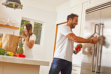 Smiling couple with paper shopping bag and groceries in kitchen