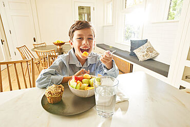 Smiling boy (8-9) enjoying breakfast in kitchen