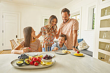 Smiling family with two children (8-9, 12-13) eating fresh fruit in kitchen