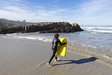 South Africa, Hermanus, Boy (10-11) entering Atlantic Ocean with body board in Kammabaai Beach