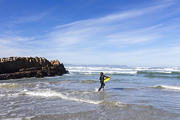 South Africa, Hermanus, Boy (10-11) entering Atlantic Ocean with body board in Kammabaai Beach