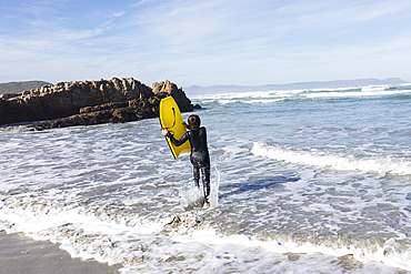 South Africa, Hermanus, Boy (10-11) entering Atlantic Ocean with body board in Kammabaai Beach