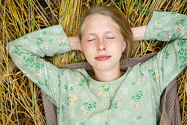 Young woman lying down in field with eyes closed 