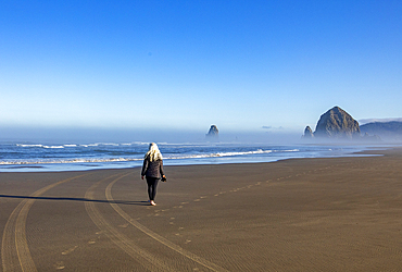 USA, Oregon, Rear view of woman walking near Haystack Rock at Cannon Beach in morning mist