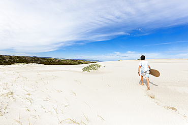 Boy (10-11) carrying surfboard in Walker Bay Nature Reserve