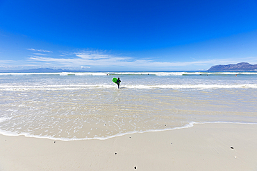 Boy (10-11) with surfboard running on empty beach