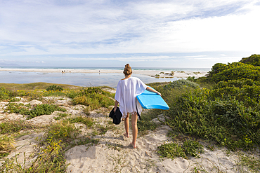 South Africa, Hermanus, Teenage girl walking on beach with body board