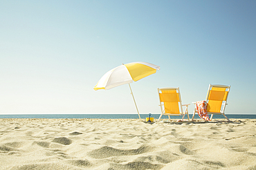 USA, Massachusetts, Nantucket, Two yellow beach chairs and umbrella on sandy beach facing ocean