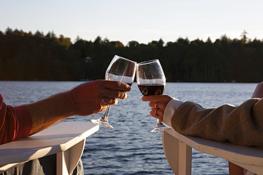 Hands of couple toasting with red wine by lake, Saranac Lake, New York, USA