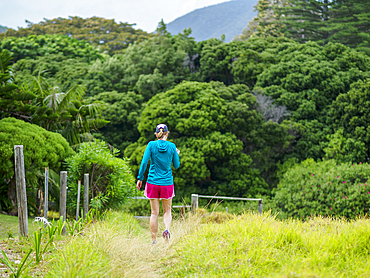 Rear view of woman walking down grassy path on Lord Howe Island, Lord Howe Island, New South Wales, Australia