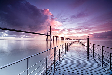 Sunrise colors the clouds reflected in Tagus River and frame the Vasco da Gama bridge in Lisbon, Portugal, Europe