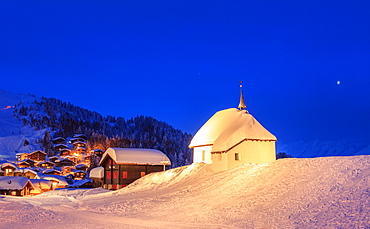 Blue dusk on the alpine village and church covered with snow, Bettmeralp, district of Raron, canton of Valais, Switzerland, Europe