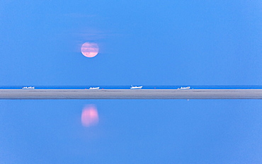 The pink full moon is reflected in the blue water of the Notteri pond, Villasimius, Province of Cagliari, Sardinia, Italy, Mediterranean, Europe