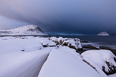 Storm clouds on the snowy peaks reflected in the cold sea at night, Haukland, Lofoten Islands, Northern Norway, Scandinavia, Europe