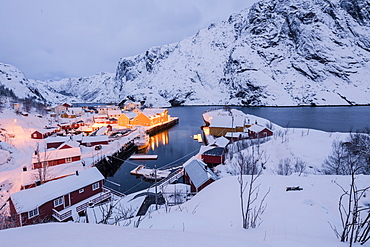 Dusk lights on the fishing village surrounded by snowy peaks, Nusfjord, Nordland, Lofoten Islands, Northern Norway, Scandinavia, Europe