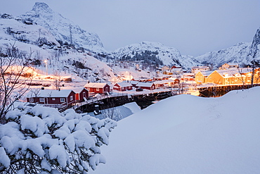 Dusk lights on the fishing village surrounded by snowy peaks, Nusfjord, Nordland, Lofoten Islands, Northern Norway, Scandinavia, Europe