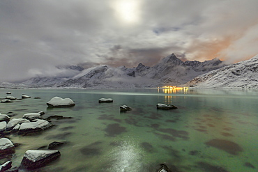 Full moon lights up the snow capped peaks reflected in the cold sea, Vareid, Flakstad, Nordland, Lofoten Islands, Northern Norway, Scandinavia, Europe