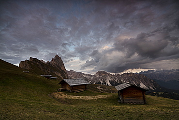 Dark clouds on green meadows and huts of the Odle mountain range seen from Seceda, Val Gardena, Trentino-Alto Adige, Italy, Europe