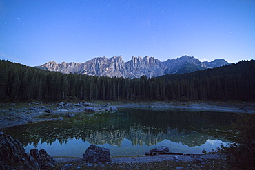 Latemar mountain range and woods are reflected in Lake Carezza at dusk, Ega Valley, Province of Bolzano, South Tyrol, Italy, Europe