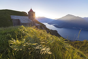 Sunbeam on Church of San Bernardo lights up the landscape around the blue water of Lake Como at dawn, Musso, Lombardy, Italy, Europe