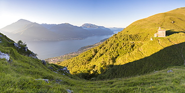 Sun on Church of San Bernardo lights up the landscape around the blue water of Lake Como at dawn, Musso, Lombardy, Italy, Europe