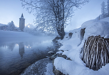 Ice and frost covering the banks of River Inn in Lower Engadine, the morning mist hiding the bell tower of the church in Sils, Graubunden, Switzerland, Europe