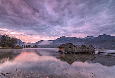 Purple sky at sunset and wooden huts are reflected in the clear water of Kochelsee, Schlehdorf, Bavaria, Germany, Europe