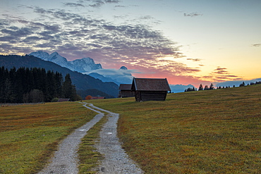 Sunset on wooden huts and meadows with the Alps in background, Geroldsee, Krun, Garmisch Partenkirchen, Upper Bavaria, Germany, Europe