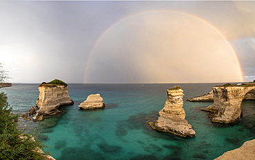 Rainbow frames rocky cliffs known as Faraglioni di Sant'andrea surrounded by turquoise sea, province of Lecce, Apulia, Italy, Europe