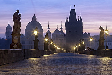 Street lanterns and old statues frame the historical buildings on Charles Bridge at dawn, UNESCO World Heritage Site, Prague, Czech Republic, Europe