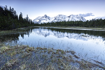 Sunrise frames the snowy peaks reflected in Lake Entova, Malenco Valley, Province of Sondrio, Valtellina, Lombardy, Italy, Europe