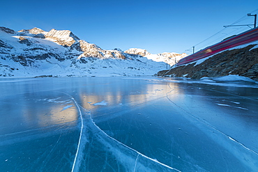 The Bernina Express train runs beside the frozen Lago Bianco, Bernina Pass, canton of Graubunden, Engadine, Switzerland, Europe