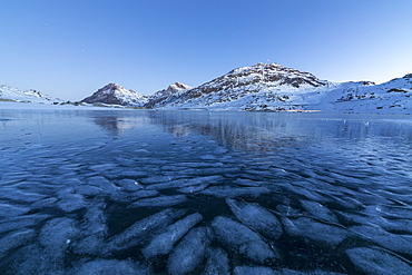 The frozen Lago Bianco framed the blue lights of dusk, Bernina Pass, canton of Graubunden, Engadine, Switzerland, Europe