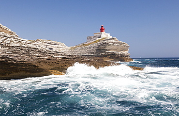 Waves of the turquoise sea crashing on the granite white cliffs and lighthouse, Lavezzi Islands, Bonifacio, Corsica, France, Mediterranean, Europe