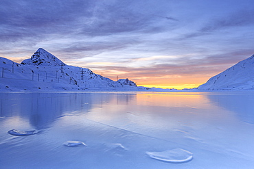 The colors of dawn invading the smooth surface of Lago Bianco exceptionally icy, Bernina Pass, Graubunden, Swiss Alps, Switzerland, Europe