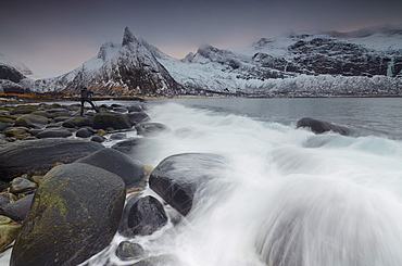 Photographer on the rocks surrounded by snowy peaks and waves of the cold sea, Senja, Ersfjord, Troms county, Norway, Scandinavia, Europe