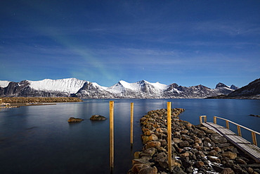 Stars of the polar night frame the frozen sea surrounded by snowy peaks, Mefjord Berg, Senja, Troms county, Norway, Scandinavia, Europe