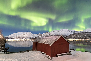 The Northern Lights (aurora borealis) reflected in the icy sea frame a typical Rorbu, Manndalen, Kafjord, Lyngen Alps, Troms, Norway, Scandinavia, Europe