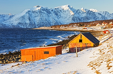 Typical wooden huts called Rorbu surrounded by waves of the cold sea and snowy peaks, Djupvik, Lyngen Alps, Troms, Norway, Scandinavia, Europe