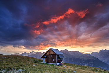 Wooden hut framed by fiery sky and clouds at sunset, Muottas Muragl, St. Moritz, Canton of Graubunden, Engadine, Switzerland, Europe