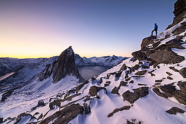 Hiker on peak Hesten admires Mount Segla and the Mefjorden framed by frozen sea at sunrise, Senja, Troms, Norway, Scandinavia, Europe