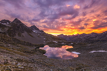 Fiery sky at dawn reflected in Lai Ghiacciato framed by peaks, Val Ursaregls, Chiavenna Valley, Valtellina, Lombardy, Italy, Europe