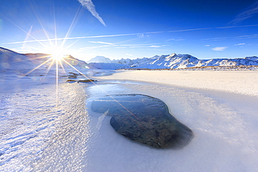 Rays of sun on the frozen Lake, Piz Umbrail framed by Mount Ortles in background, Braulio Valley, Valtellina, Lombardy, Italy, Europe