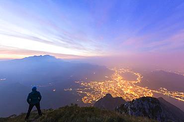 Hiker on Monte Coltignone looks toward Monte Resegone and Lecco at dawn, Lombardy, Italian Alps, Italy, Europe