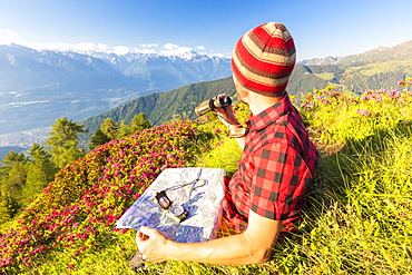 Hiker with map and binoculars looks towards Rhaetian Alps and Monte Disgrazia from Pizzo Berro, Bitto Valley, Lombardy, Italy, Europe