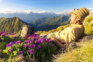 Man lying down on top of Monte Azzarini looks to Monte Disgrazia and Monte Pedena, Albaredo Valley, Orobie Alps, Lombardy, Italy, Europe