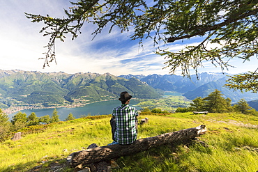 Man sitting on tree trunk looks towards Lake Como and Alto Lario, Monte Legnoncino, Lecco province, Lombardy, Italy, Europe