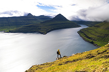 Hiker on rocks looks at the fjords, Funningur, Eysturoy island, Faroe Islands, Denmark, Europe